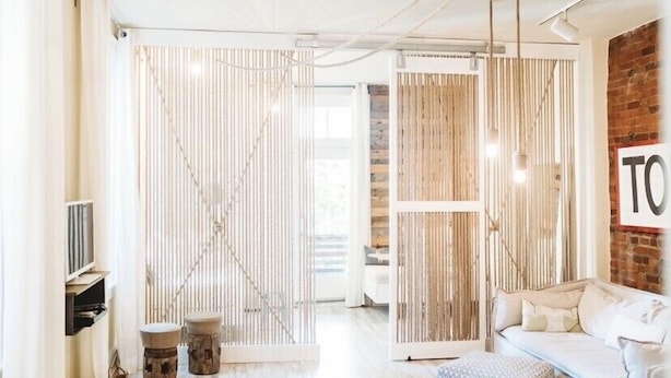 Un salon moderne avec un canapé blanc, une cloison en bois et un téléviseur posé sur une étagère.