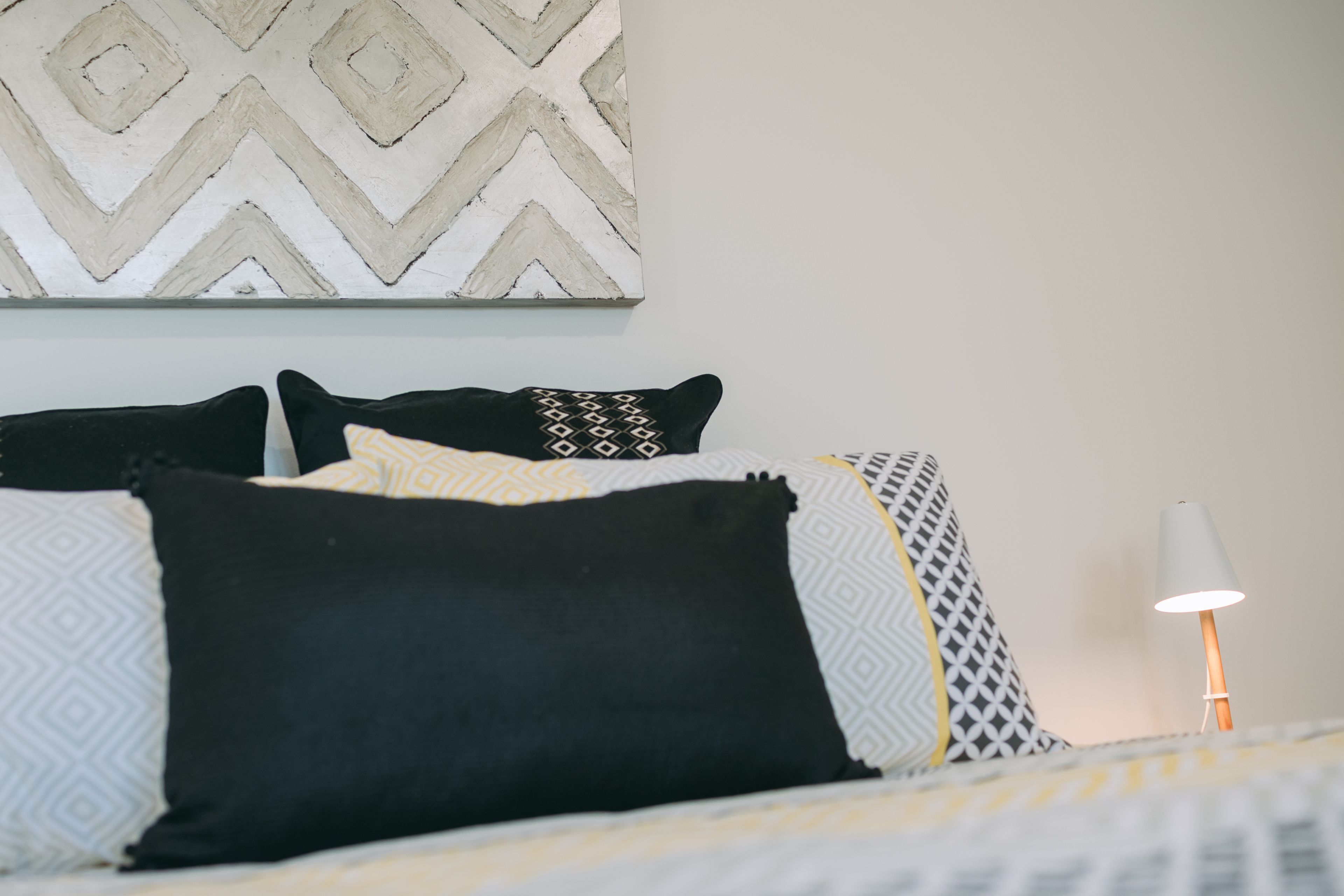 A neatly made bed with patterned pillows and a bedside lamp.