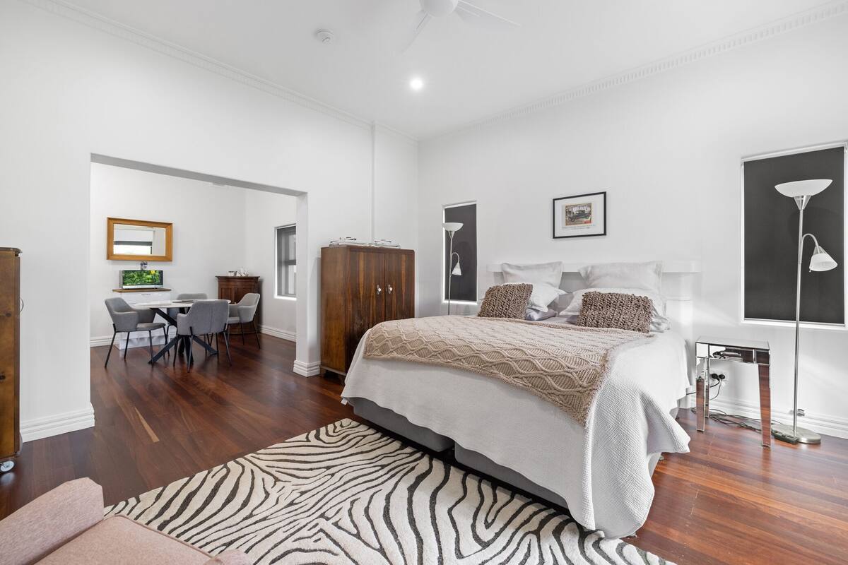 A spacious bedroom with a large bed, a desk with chairs, and a wardrobe.