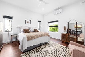 Quarto moderno com cama, penteadeira, espelho e vista para o verde lá fora.
