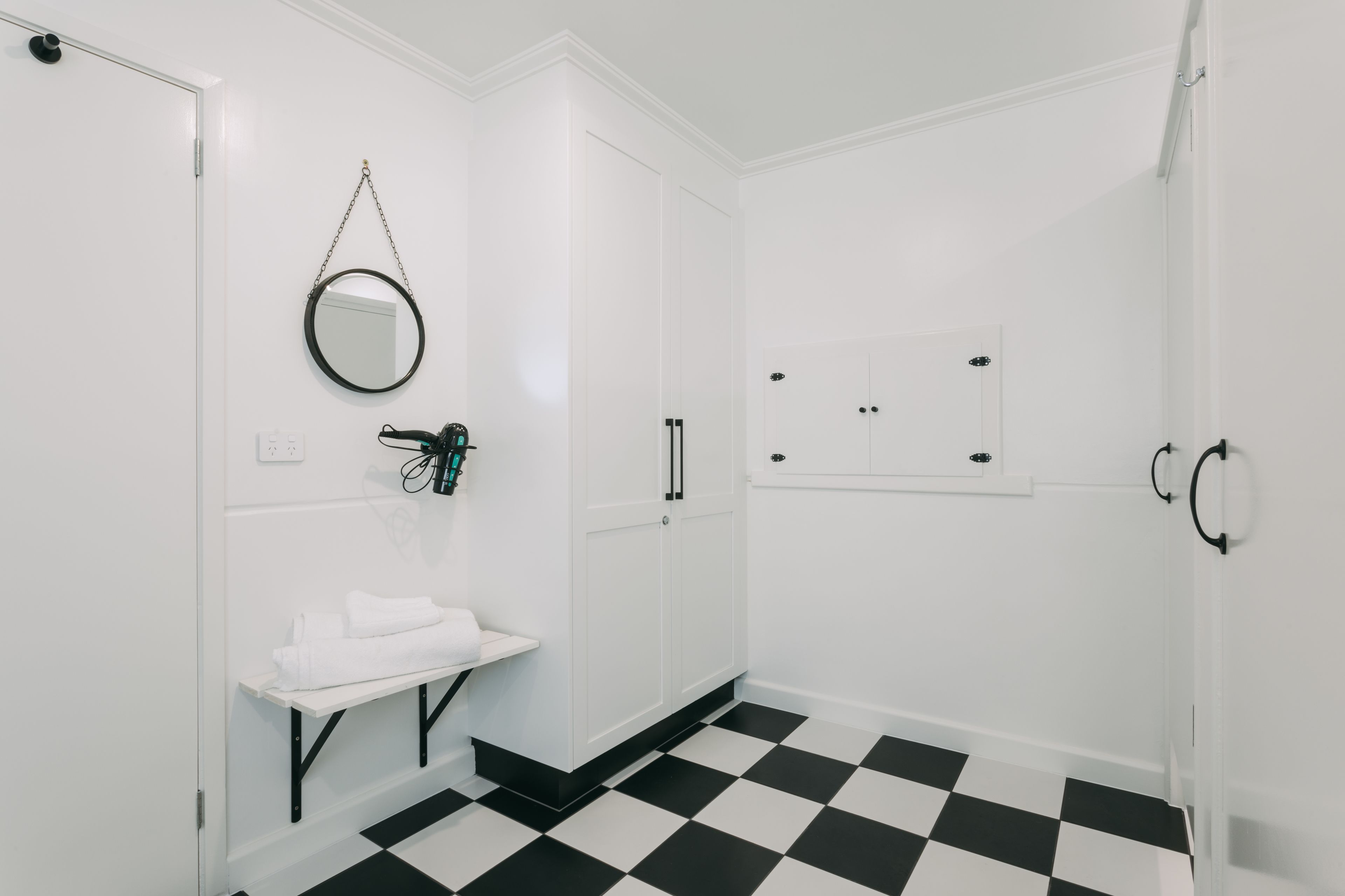 A bathroom with a black and white checkered floor, a white sink with a mirror above it, and a small shelf with towels.