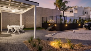 A covered patio with outdoor furniture, a staircase leading to a second floor, and a landscaped garden area.