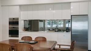 A modern kitchen with white cabinetry, stainless steel appliances, a dining table with chairs, and a refrigerator.