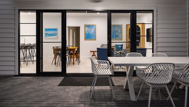 A modern dining area with a white table and chairs, a ceiling fan, and a view through glass doors into a dining space with chairs and tables.