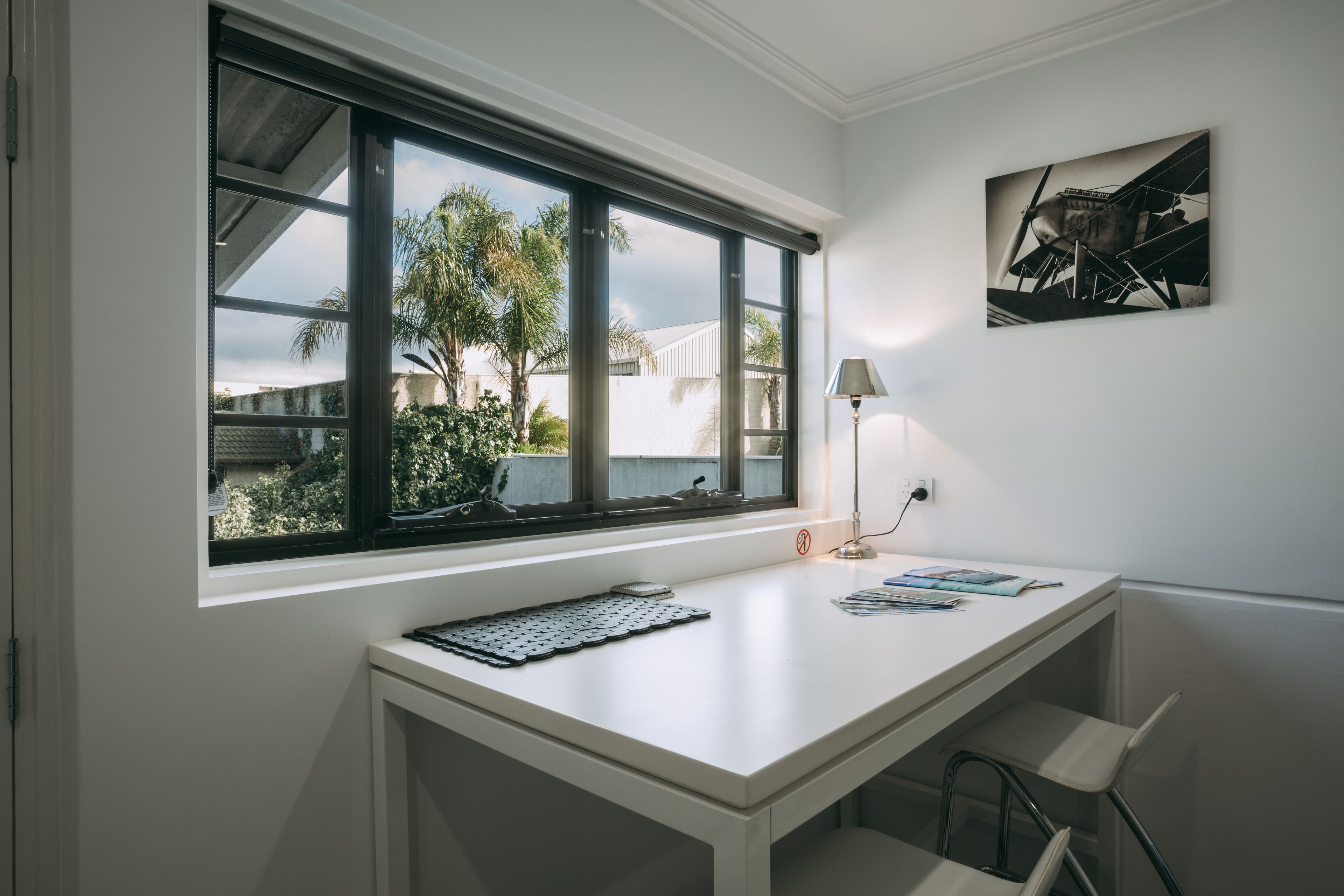 A modern office space with a large window, a desk, a chair, a lamp, and a framed picture on the wall.
