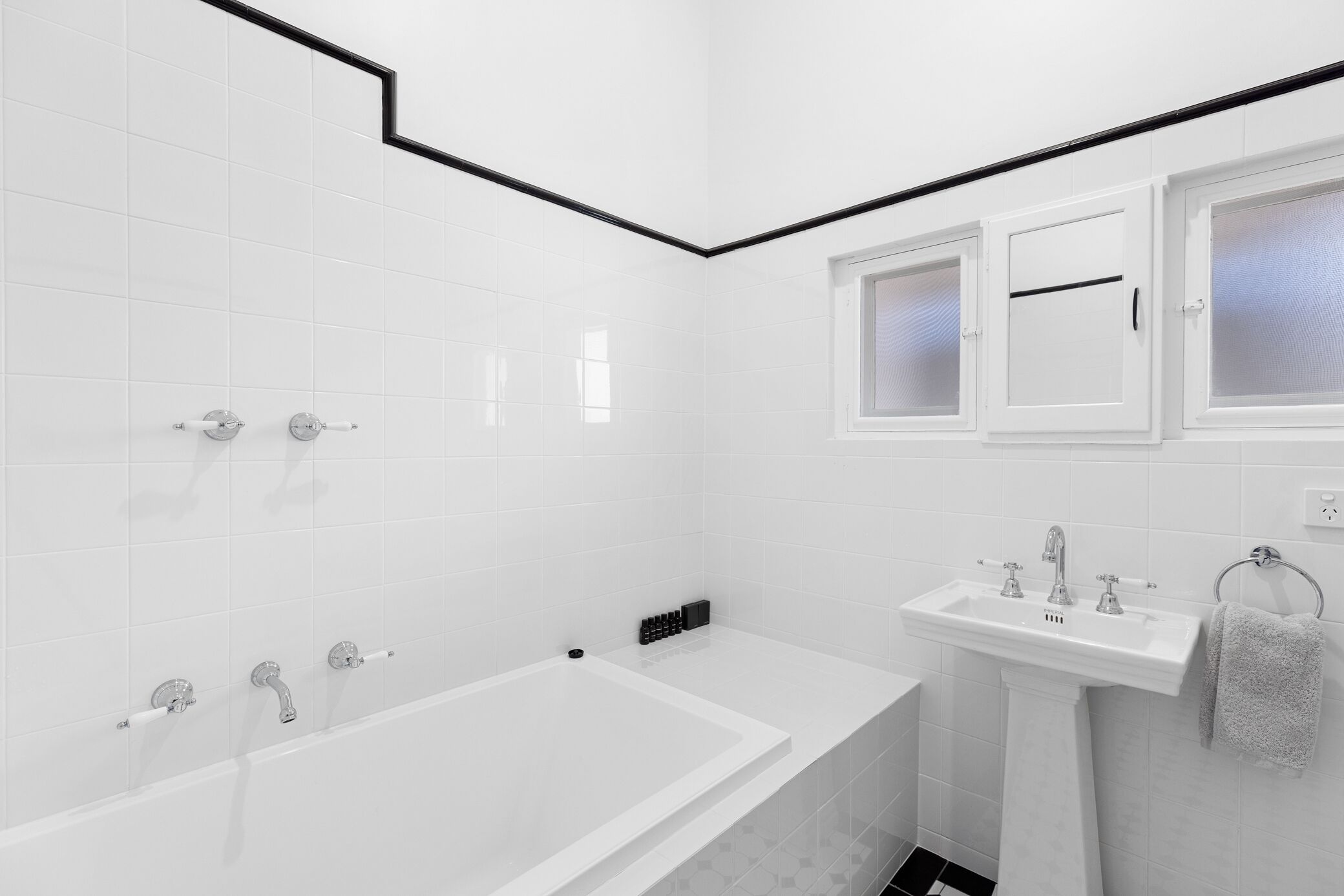 Un baño moderno con azulejos blancos, una bañera, un lavamanos y un ventanal con vidrio esmerilado.