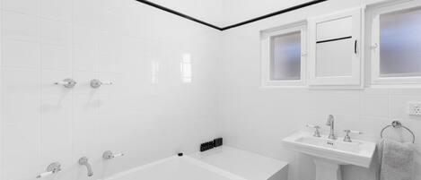 Un baño moderno con azulejos blancos, una bañera, un lavamanos y un ventanal con vidrio esmerilado.