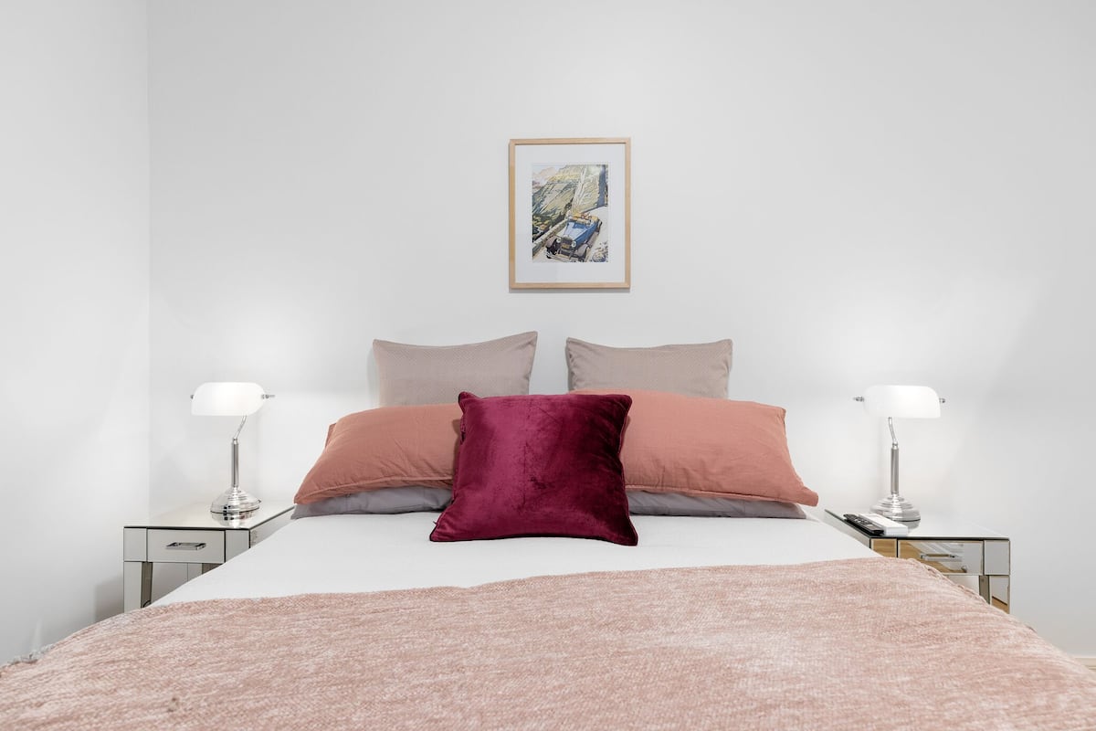 A neatly made bed with a pink blanket, two bedside lamps, and a framed picture on the wall.