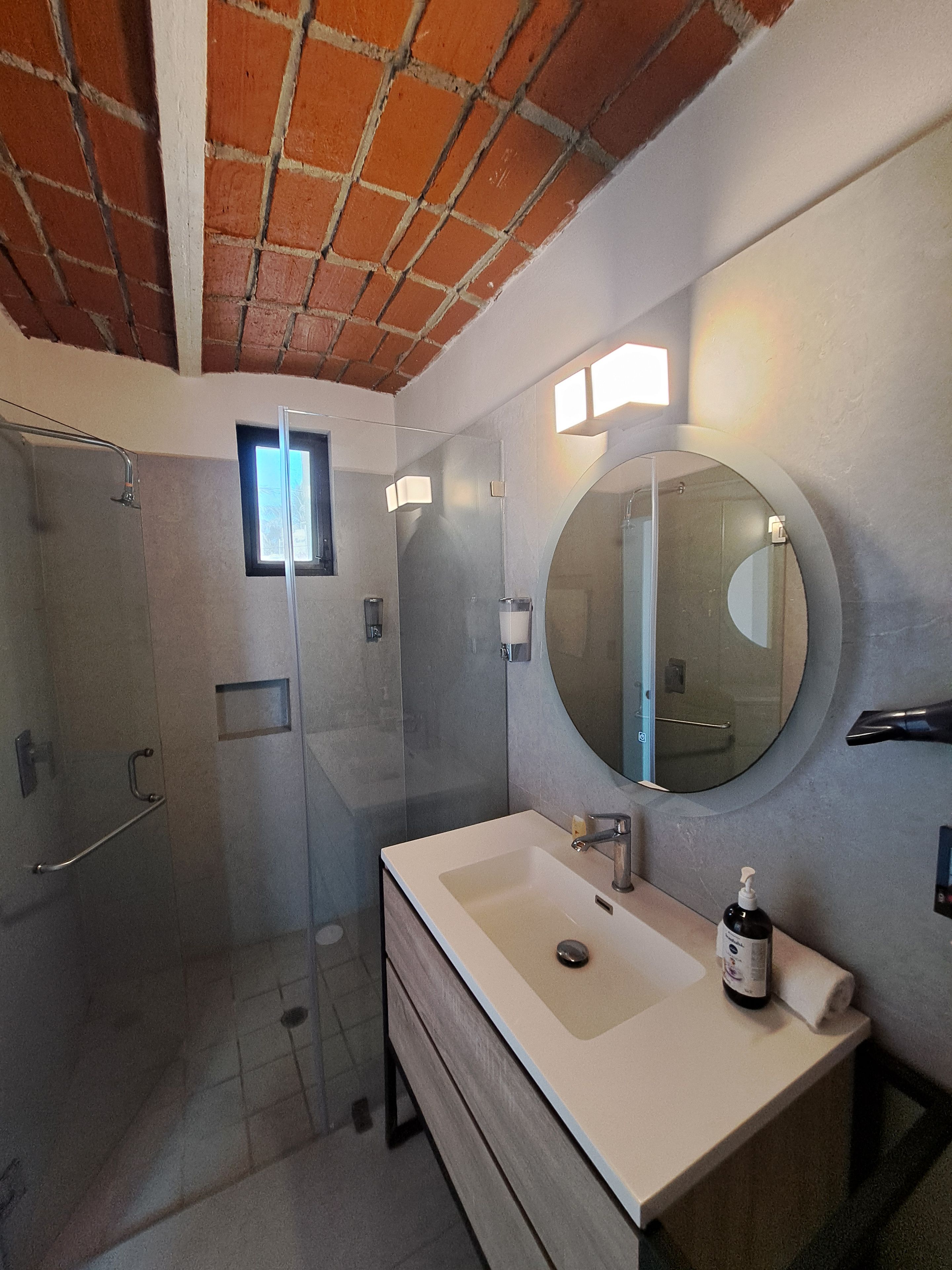 Un baño moderno con ducha de vidrio, espejo redondo y lavamanos blanco.