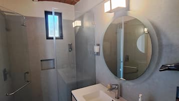 Un baño moderno con ducha de vidrio, espejo redondo y lavamanos blanco.