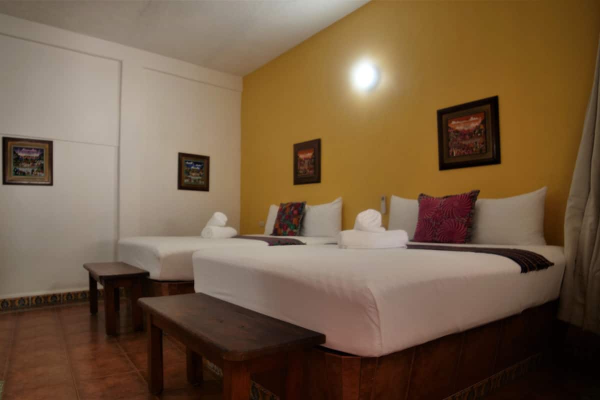 Quarto de hotel com duas camas, um banco e uma pequena mesa.