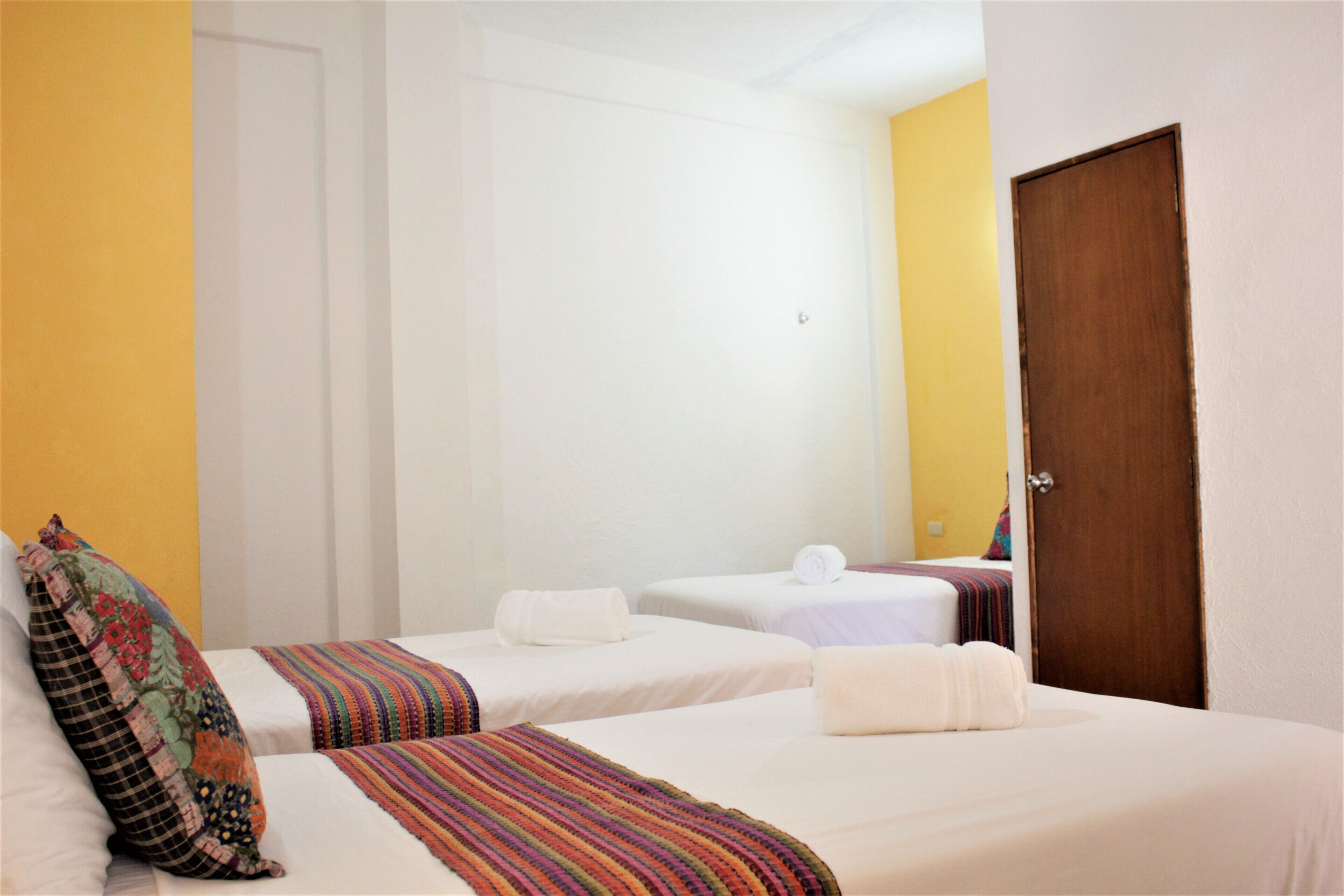 A hotel room with two single beds, a wooden door, and a yellow accent wall.