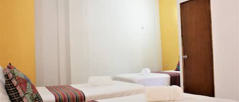 A hotel room with two single beds, a wooden door, and a yellow accent wall.