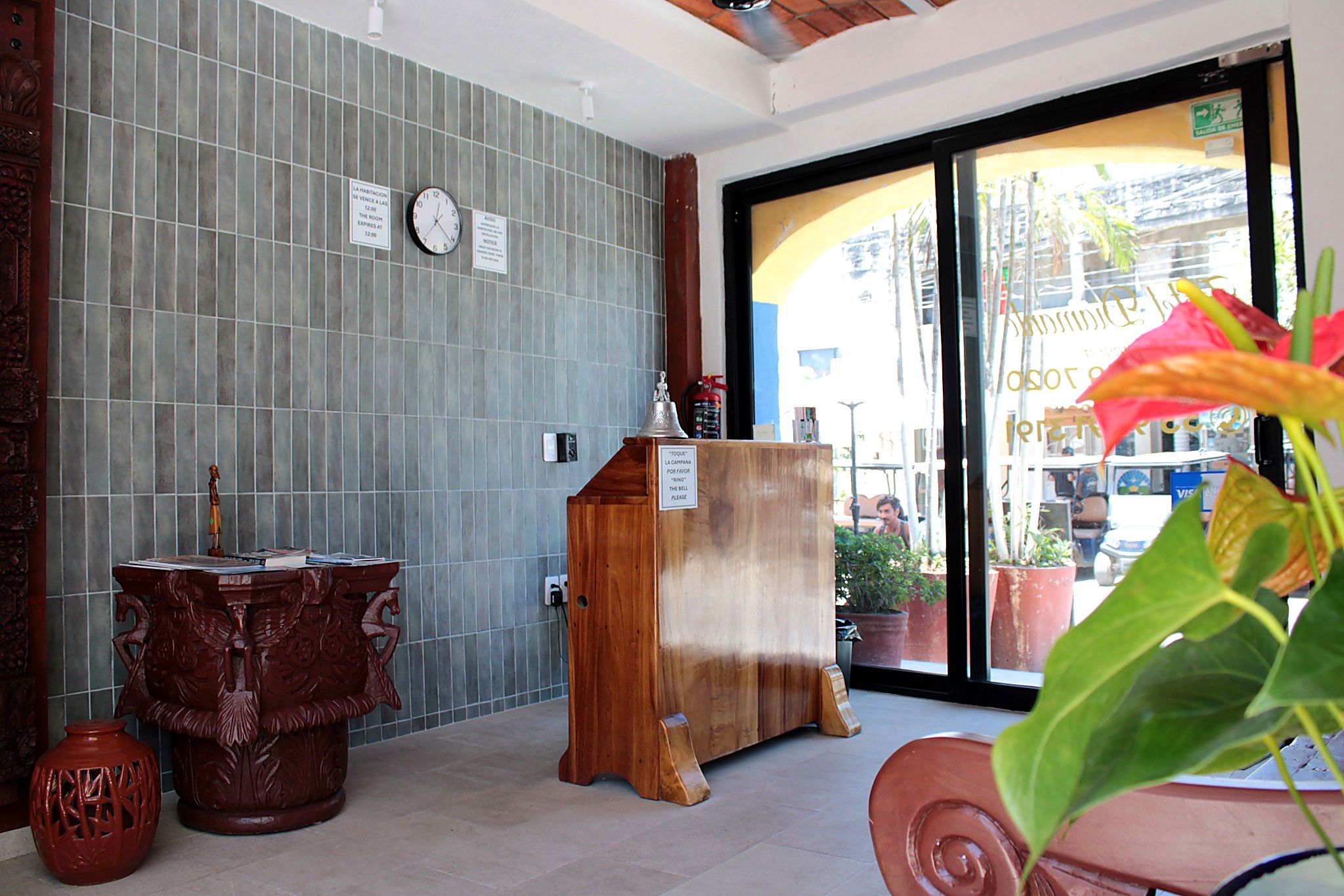 A reception area with a tiled wall, a wooden desk, a clock, and a window with a view of the outside.