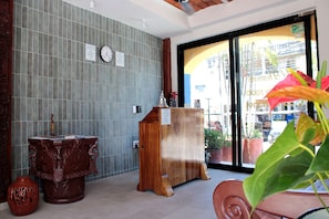 A reception area with a tiled wall, a wooden desk, a clock, and a window with a view of the outside.