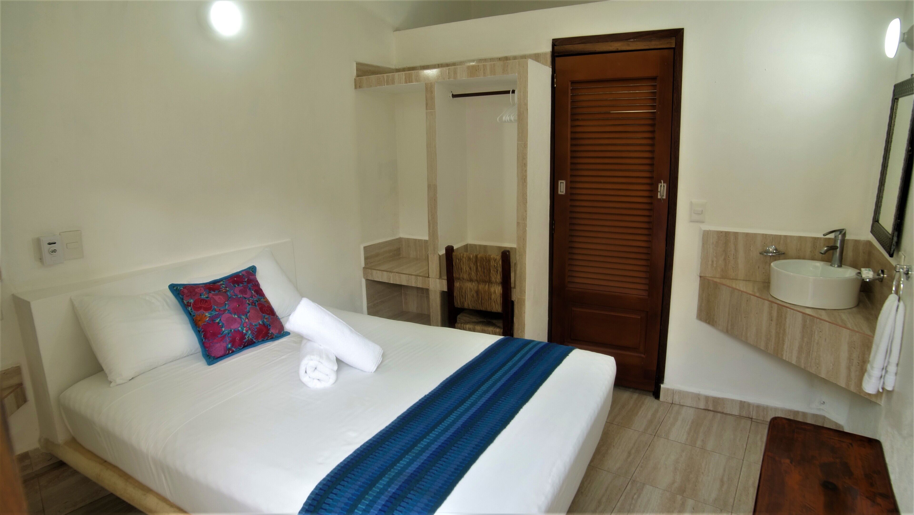 Habitación de hotel con cama, baño con lavabo y espejo, y puerta de madera.