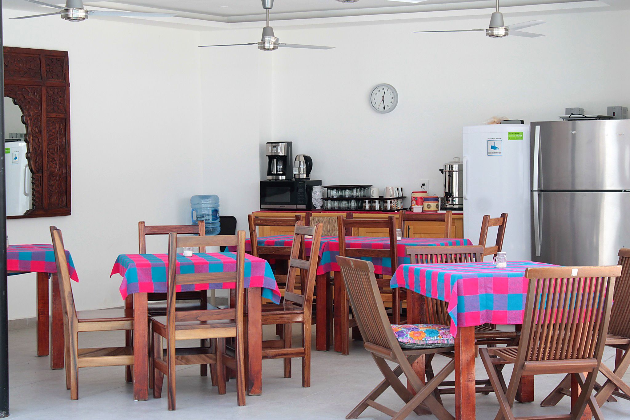 A dining area with wooden chairs and tables, a kitchen with appliances, and a ceiling fan.