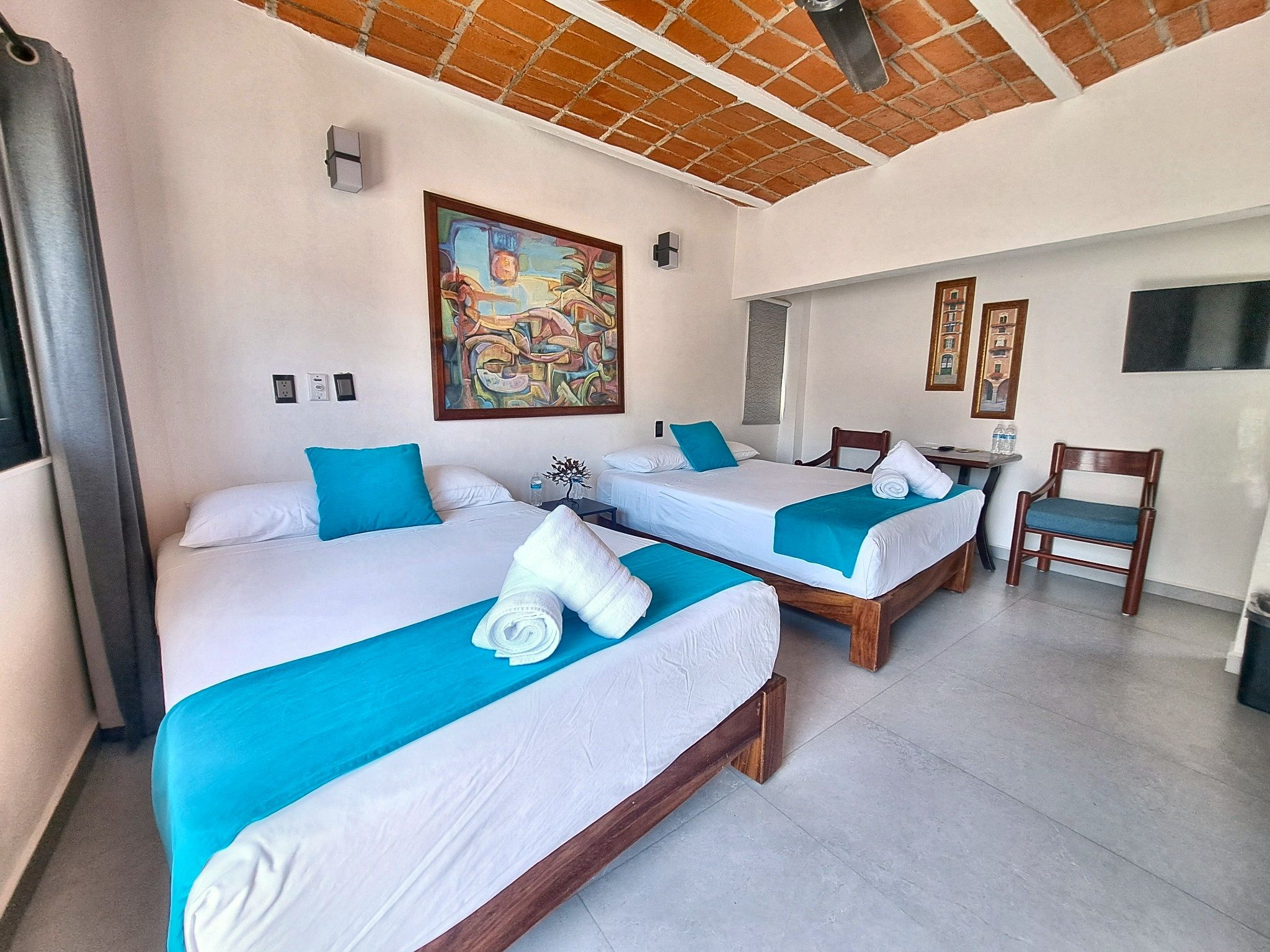 A hotel room with two beds, a painting on the wall, a small table, and a chair.