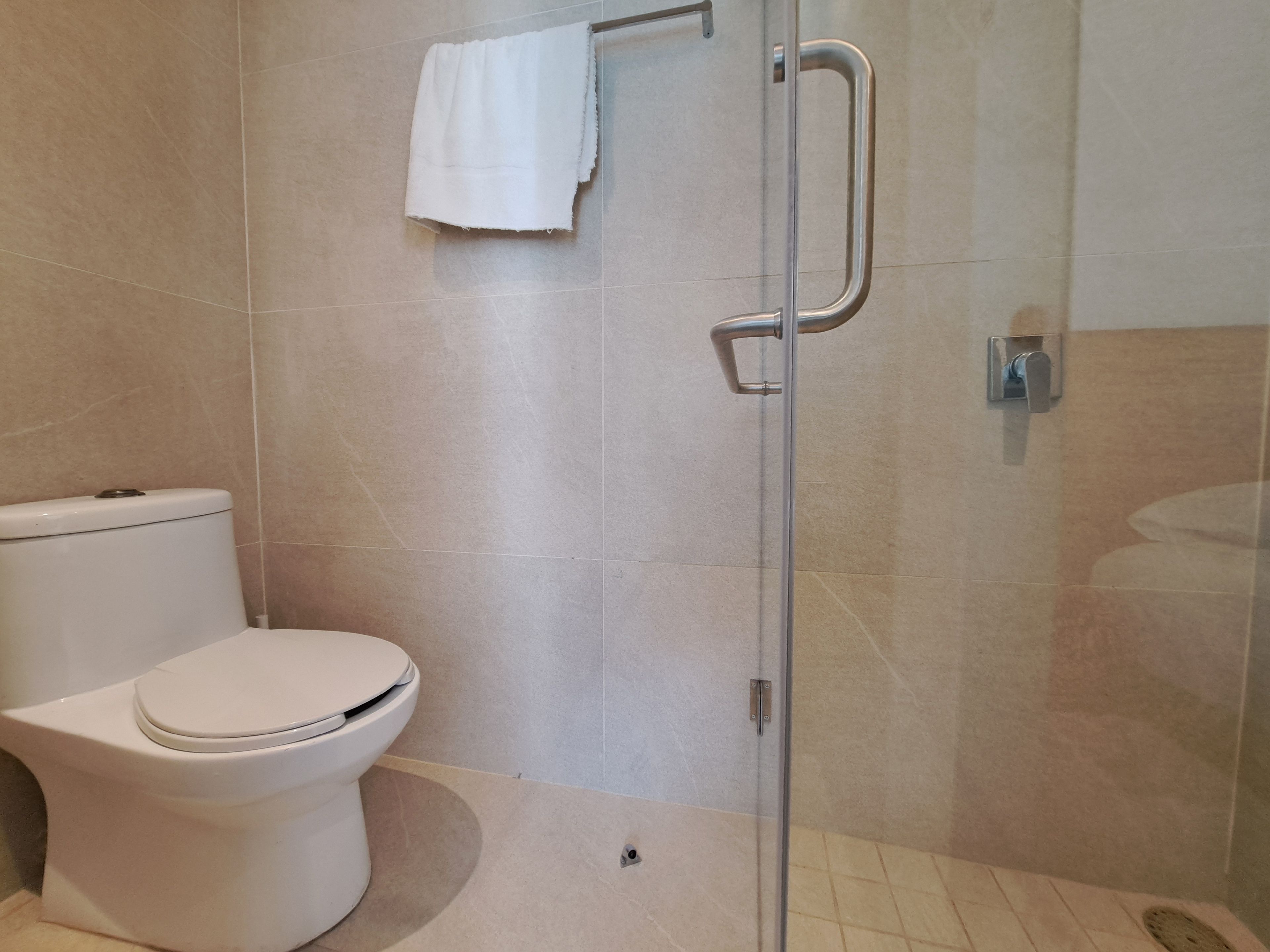 Un baño con inodoro, cabina de ducha de vidrio y una toalla colgada en la pared.