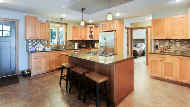 A spacious kitchen with wooden cabinets, a central island with stools, and a stainless steel refrigerator. - Beautiful Get Away for any season only ONE Hour from the Twin Cities! (Zimmerman)