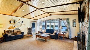 A cozy living room with a wooden ceiling, a blue sofa, a wooden coffee table, and a stone wall. - Beautiful Get Away for any season only ONE Hour from the Twin Cities! (Zimmerman)