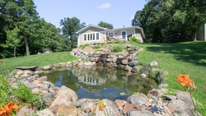 A house with a pond, surrounded by rocks and greenery. - Beautiful Get Away for any season only ONE Hour from the Twin Cities! (Zimmerman)