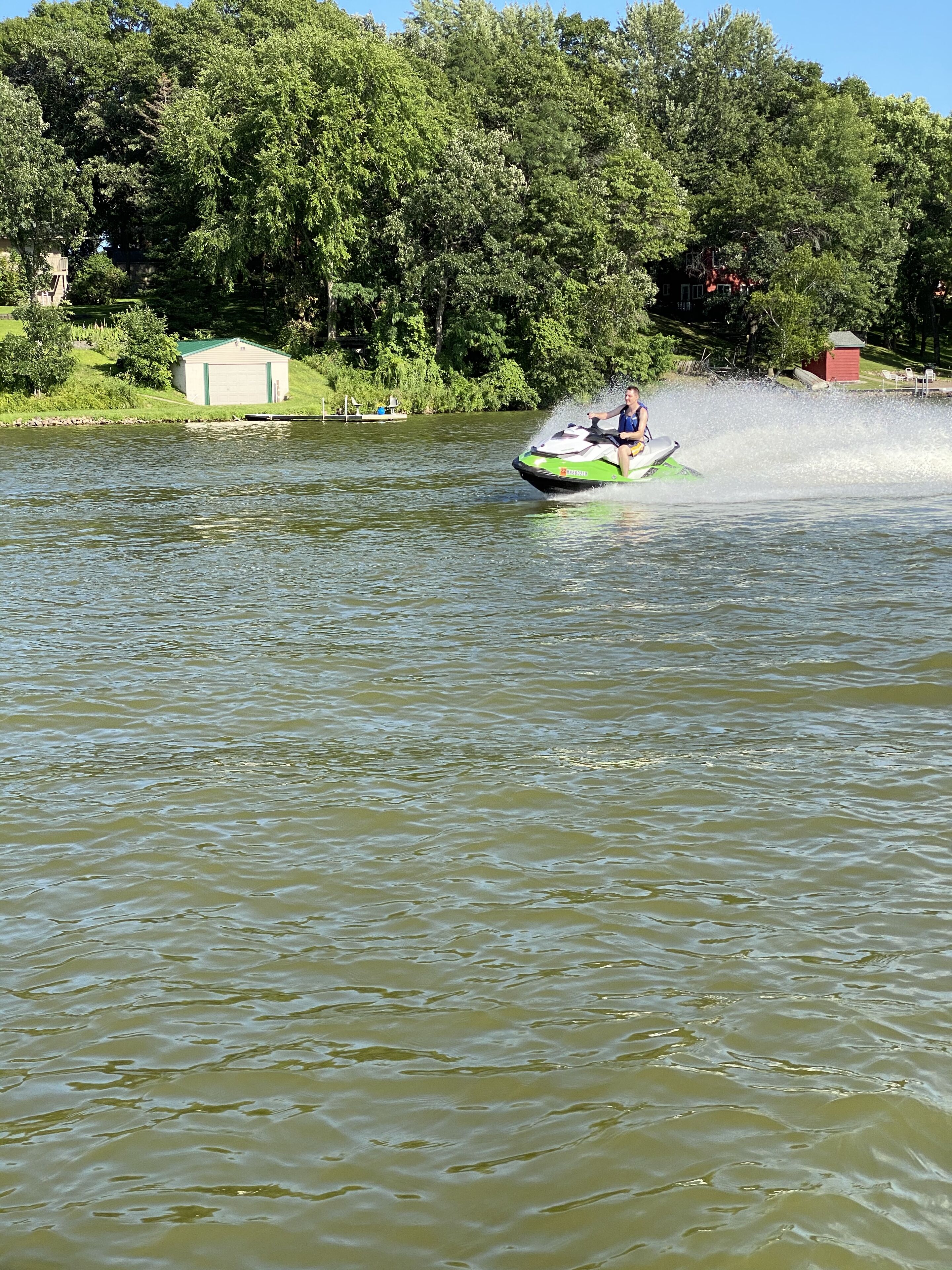A green and white jet ski on a body of water with a dock and buildings in the background.