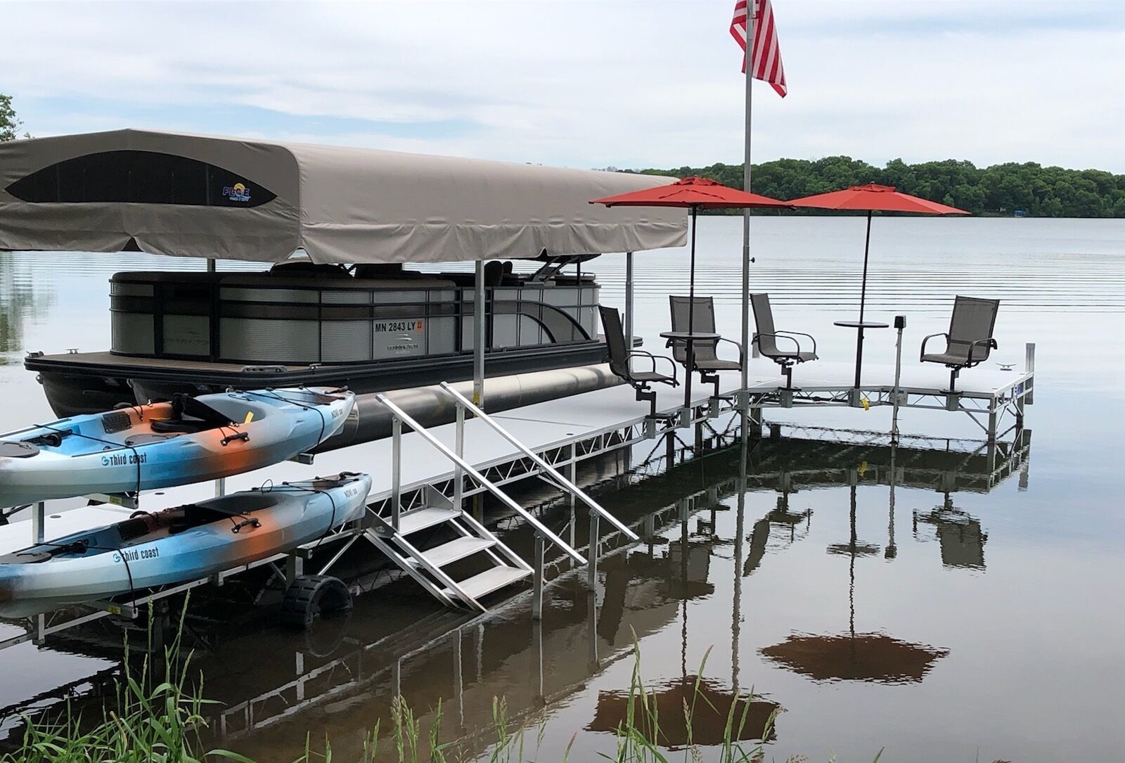 Un muelle con kayaks, una zona de estar techada y una bandera estadounidense.