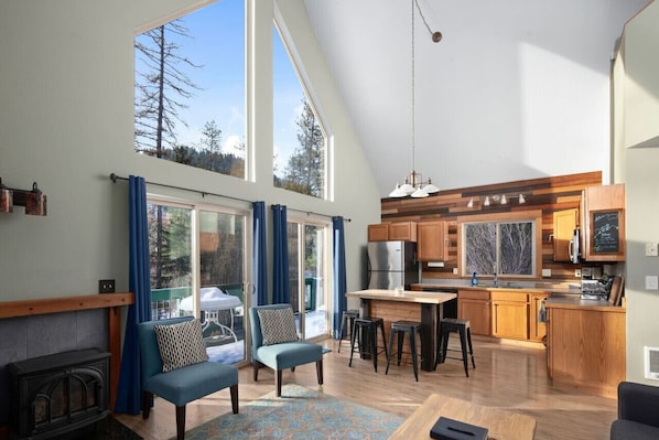 A spacious living area with a large window, a fireplace, a sofa, and a kitchen with wooden cabinets and a dining area.