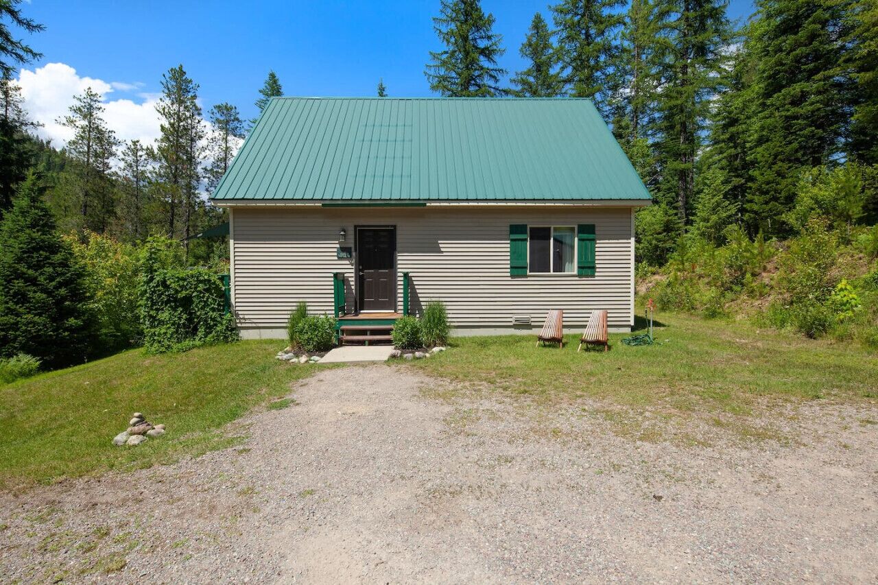 A small, single-story cabin with a green roof, surrounded by a forest.