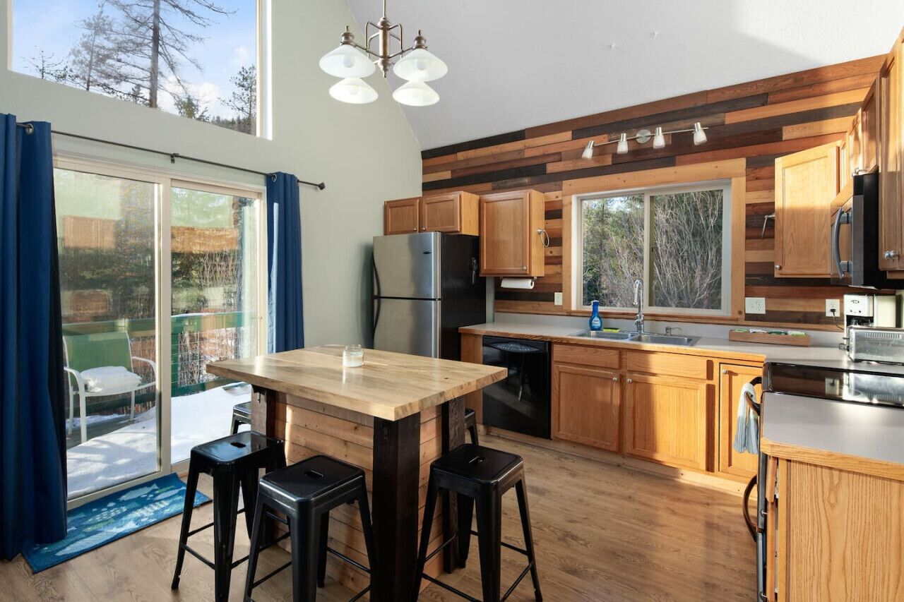 A modern kitchen with wooden cabinets, a stainless steel refrigerator, and a large window overlooking a deck.