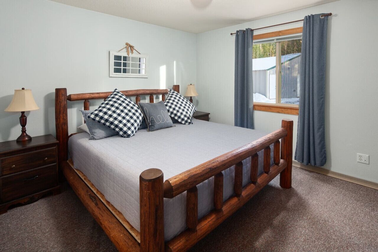 A bedroom with a wooden bed, two bedside tables, a window with curtains, and a wall-mounted picture.