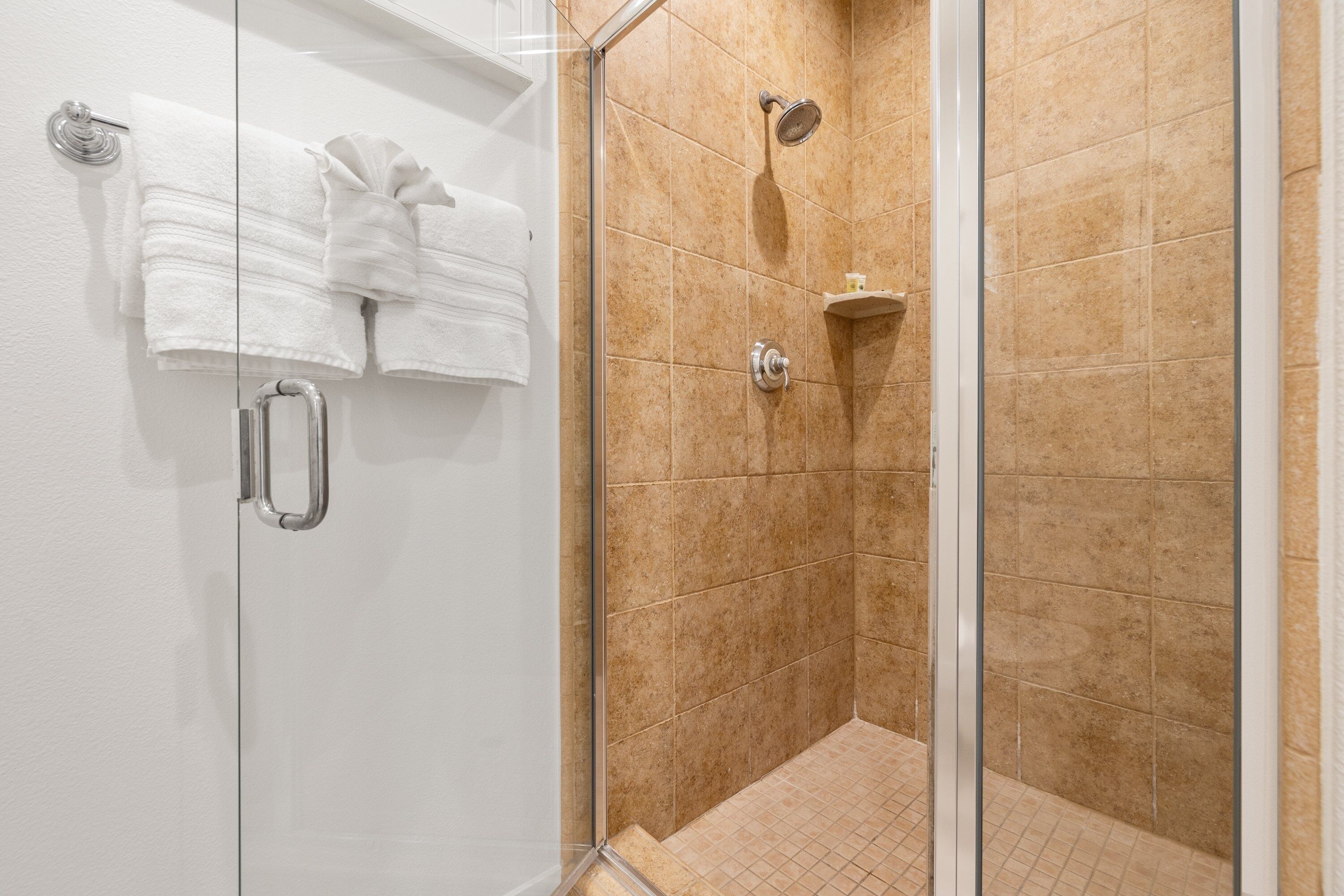 A glass-enclosed shower area with beige tiles, a glass door, and a towel rack with folded towels.