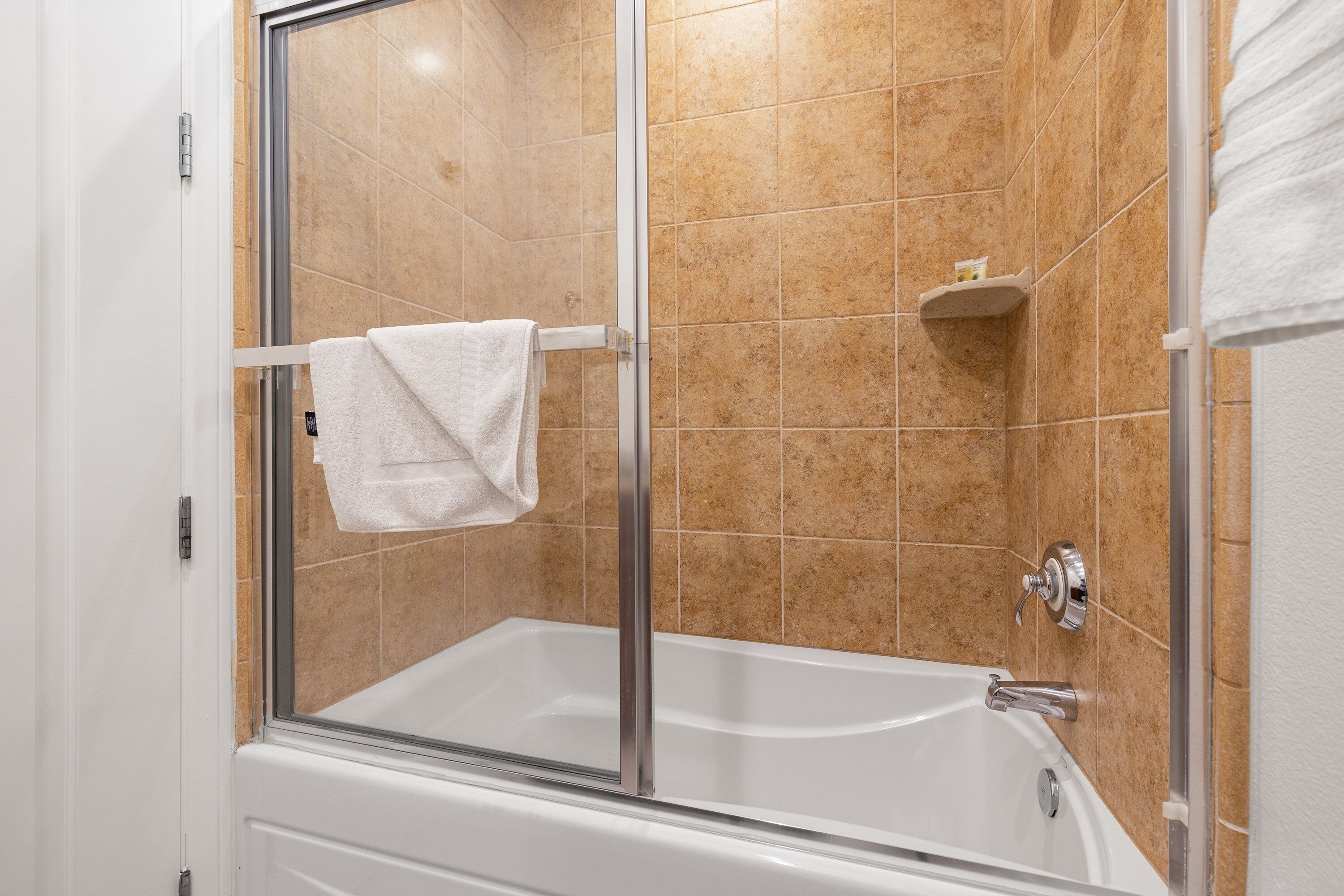 A shower with a glass door, a white bathtub, and beige tiled walls.