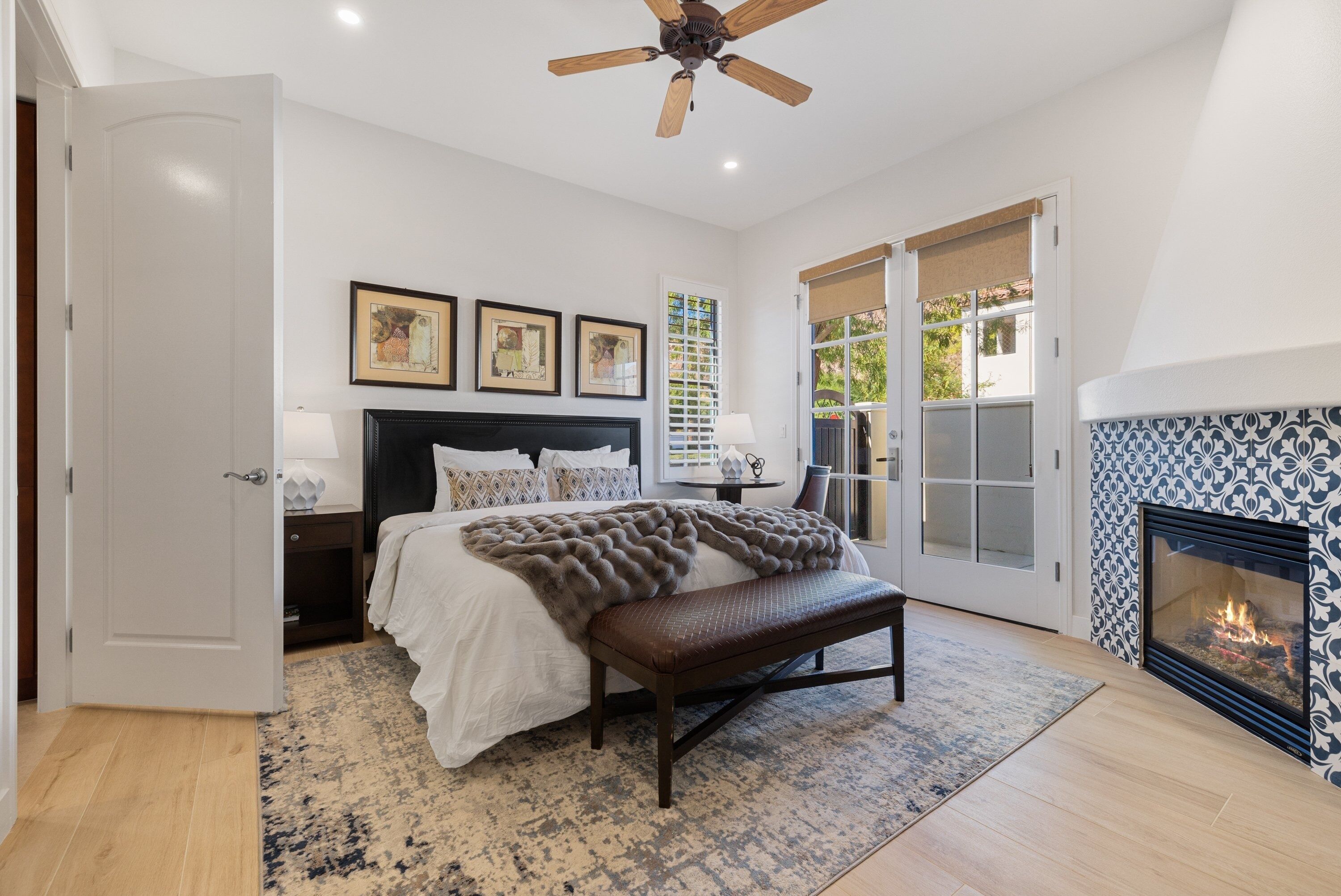 A bedroom with a bed, a bench, a fireplace, and a ceiling fan.