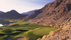 A golf course with a lake, surrounded by mountains.