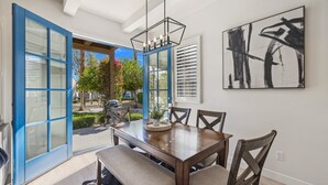 A dining area with a wooden table and chairs, a hanging light fixture, and a large abstract painting on the wall.