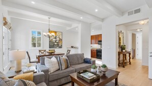A spacious living room with a grey sofa, wooden coffee table, and a dining area with a chandelier. - Heritage 3 Bedrooms H90 by RedAwning (La Quinta)