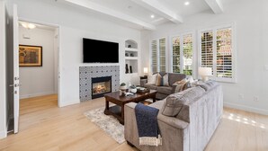 A modern living room with a fireplace, a sofa, a coffee table, and a TV mounted on the wall. - Heritage 3 Bedrooms H90 by RedAwning (La Quinta)
