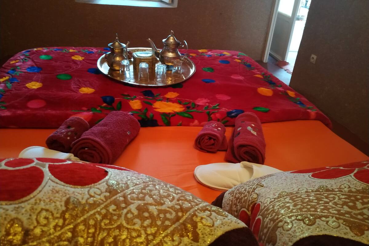 A neatly arranged room with a red floral bedspread, a tray with tea set, and rolled towels.