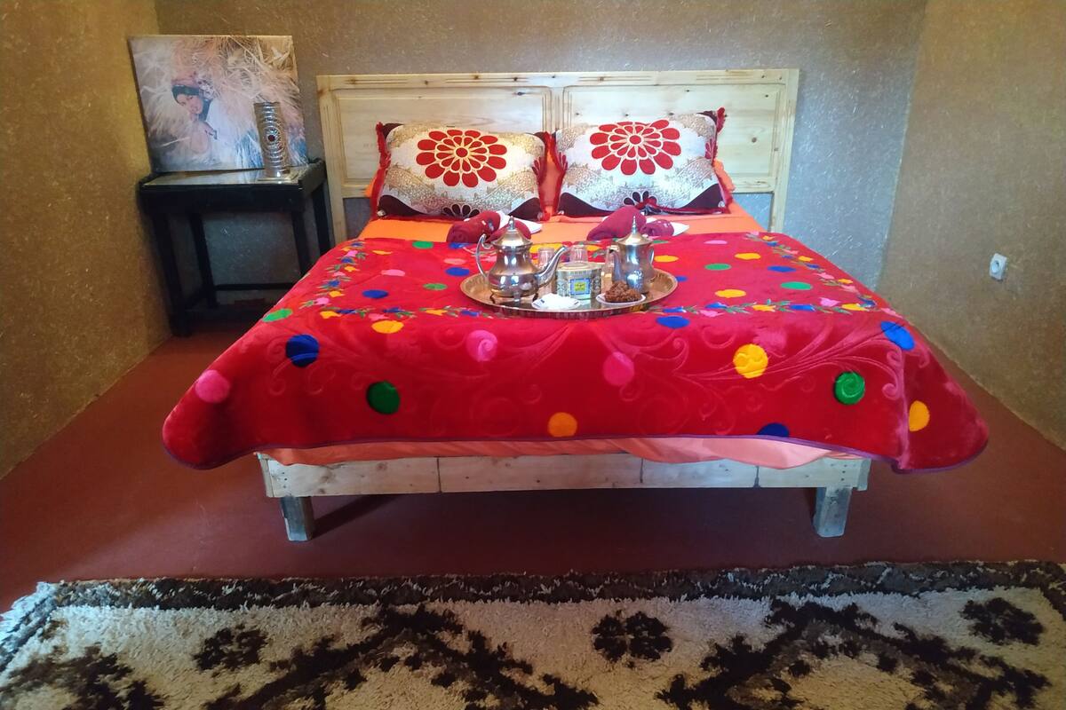 A bed with a red polka dot bedspread, two pillows with floral designs, and a tray with a teapot and cups on the headboard.