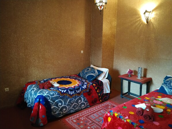 Habitación con dos camas, cada una con ropa de cama estampada, una mesita con un florero y luces fijadas en la pared.