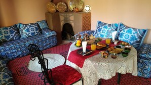 A traditional Moroccan setting with patterned cushions, a low table set with food and drinks, and a decorative wall. - Riad Dar Zaouia (Zagora)