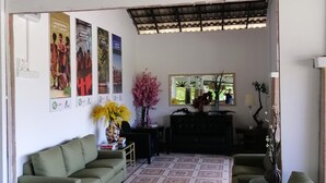 A living room with a green sofa, a coffee table, and a painting of a landscape. There are posters on the wall and a window with a view of trees. - AsiaCamp Resort (Kuala Tembeling)
