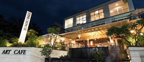 A modern building with a sign reading "BUMPI BALI ART CAFE" and a well-lit entrance with outdoor seating.