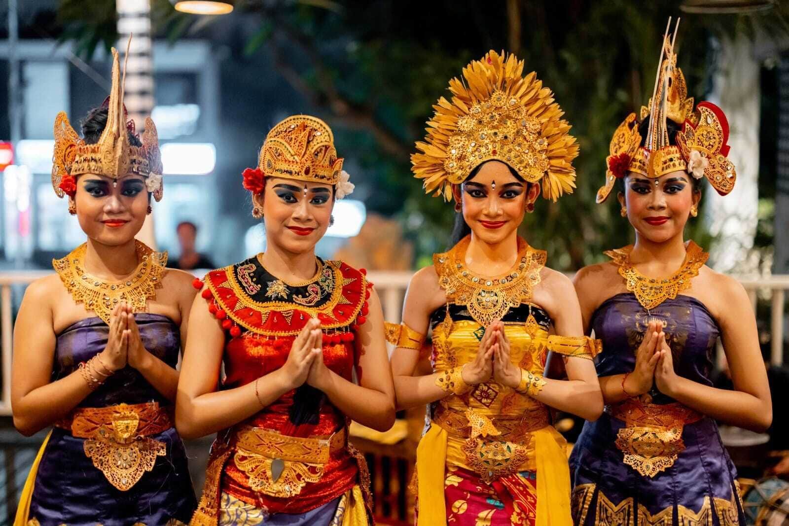Four individuals in traditional attire with elaborate headdresses and jewelry, standing in a line.