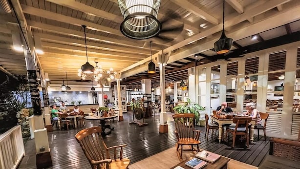 A spacious indoor area with wooden flooring, multiple seating arrangements, and hanging pendant lights.