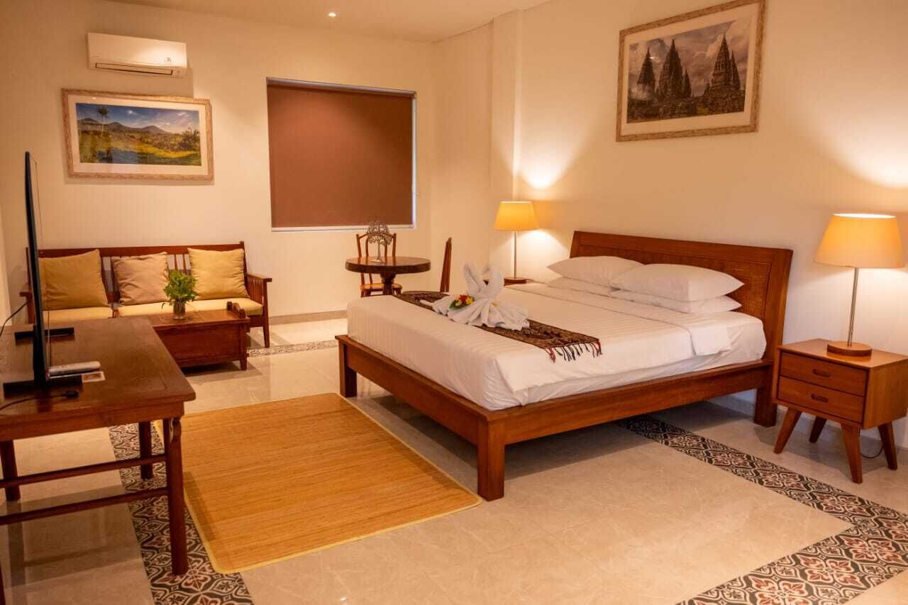 Ein Hotelzimmer mit einem hölzernen Bett, einem Schreibtisch, einem Sessel, einem kleinen Tisch und einem Fernseher.