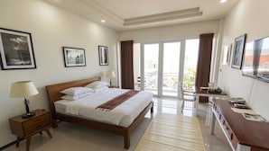 A hotel bedroom with a bed, bedside tables, a desk, and a balcony with a view.