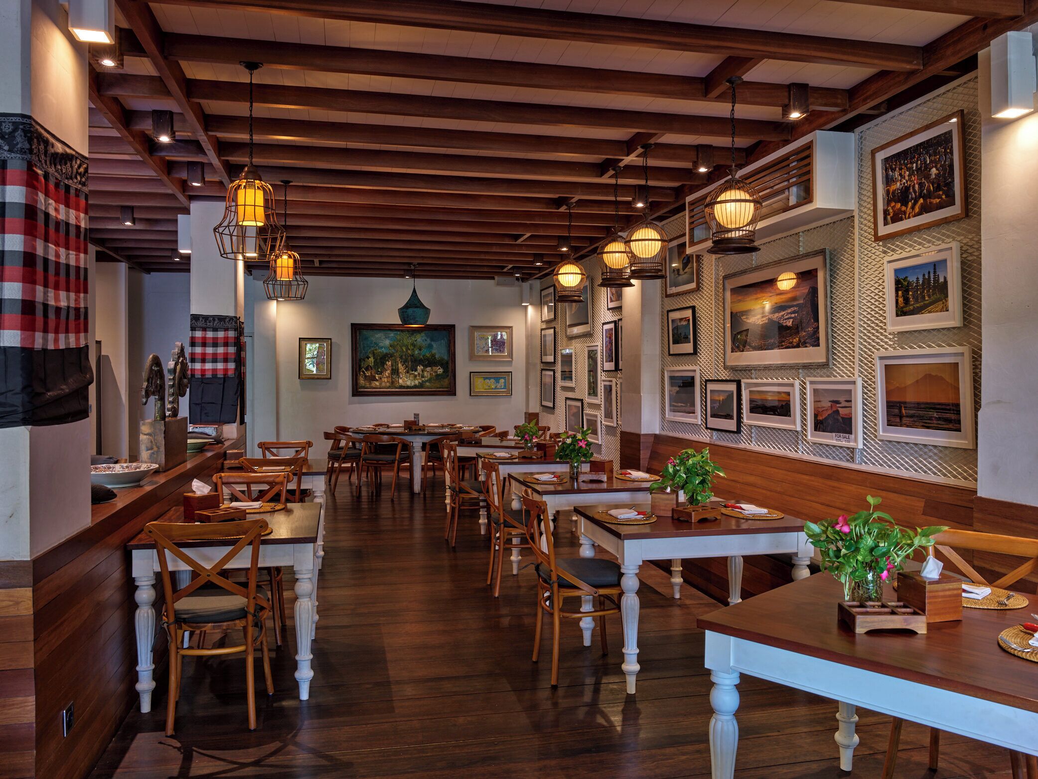 Un restaurante con mesas y sillas de madera, lámparas colgantes y cuadros en las paredes.